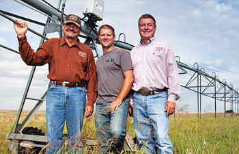 Johnny, Justin, and Joe Freeman in front of a giant piece of farm equipment.