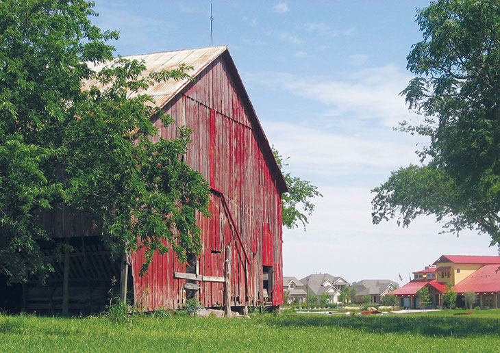 Cool-looking old red barn on green grass with trees