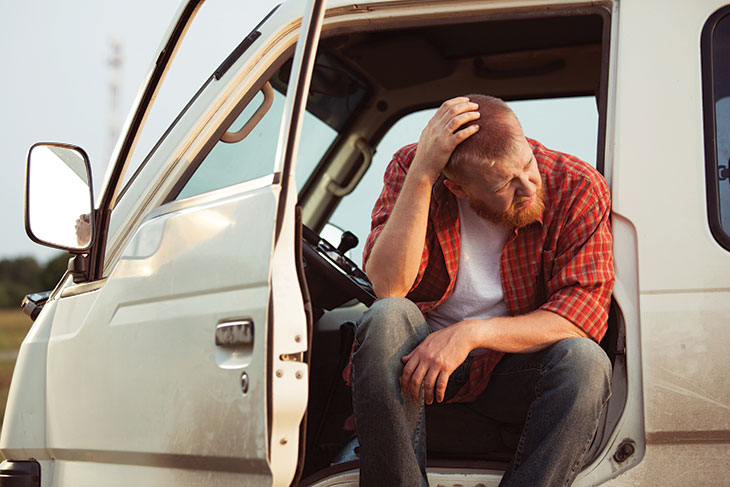 Worried farmer sits with car door open