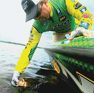 Tim Horton lean over the side of a boat and holds a fish in the water